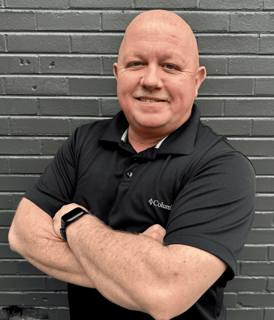 A man with his arms crossed standing in front of a brick wall.